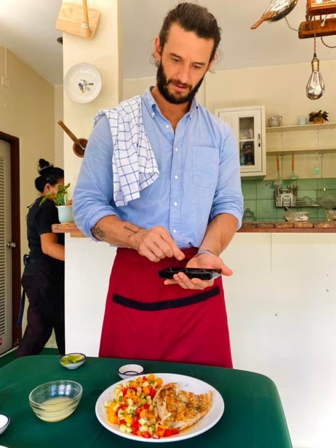 Man in blue shirt tying red apron in kitchen over prepared food plate