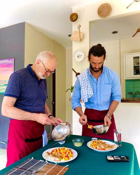 Two men cooking together in a kitchen, plating food onto white plates on a green table