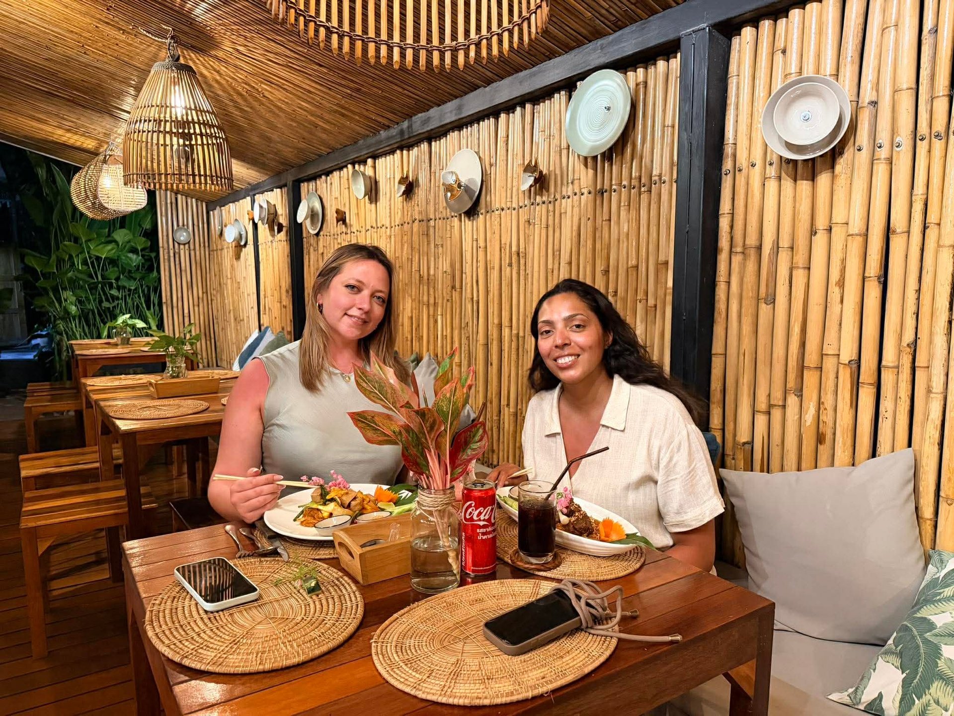 Two women dining together at a wooden table in a modern restaurant with bamboo wall decor and hanging plates
